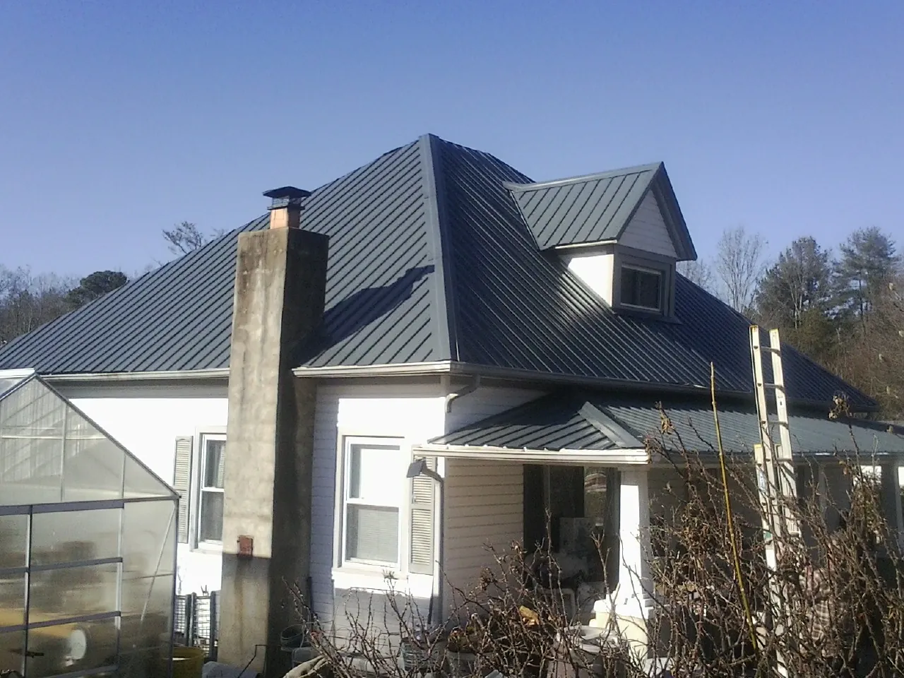 Dark blue standing seam metal roof on a white farmhouse with dormer — Slate & Tile Roof Repair by Roofing Brothers in Alpha